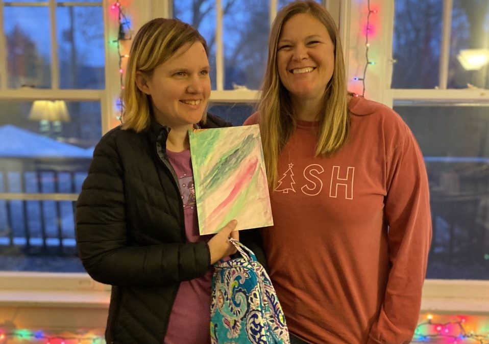 Two women standing next to each other holding up a small painting